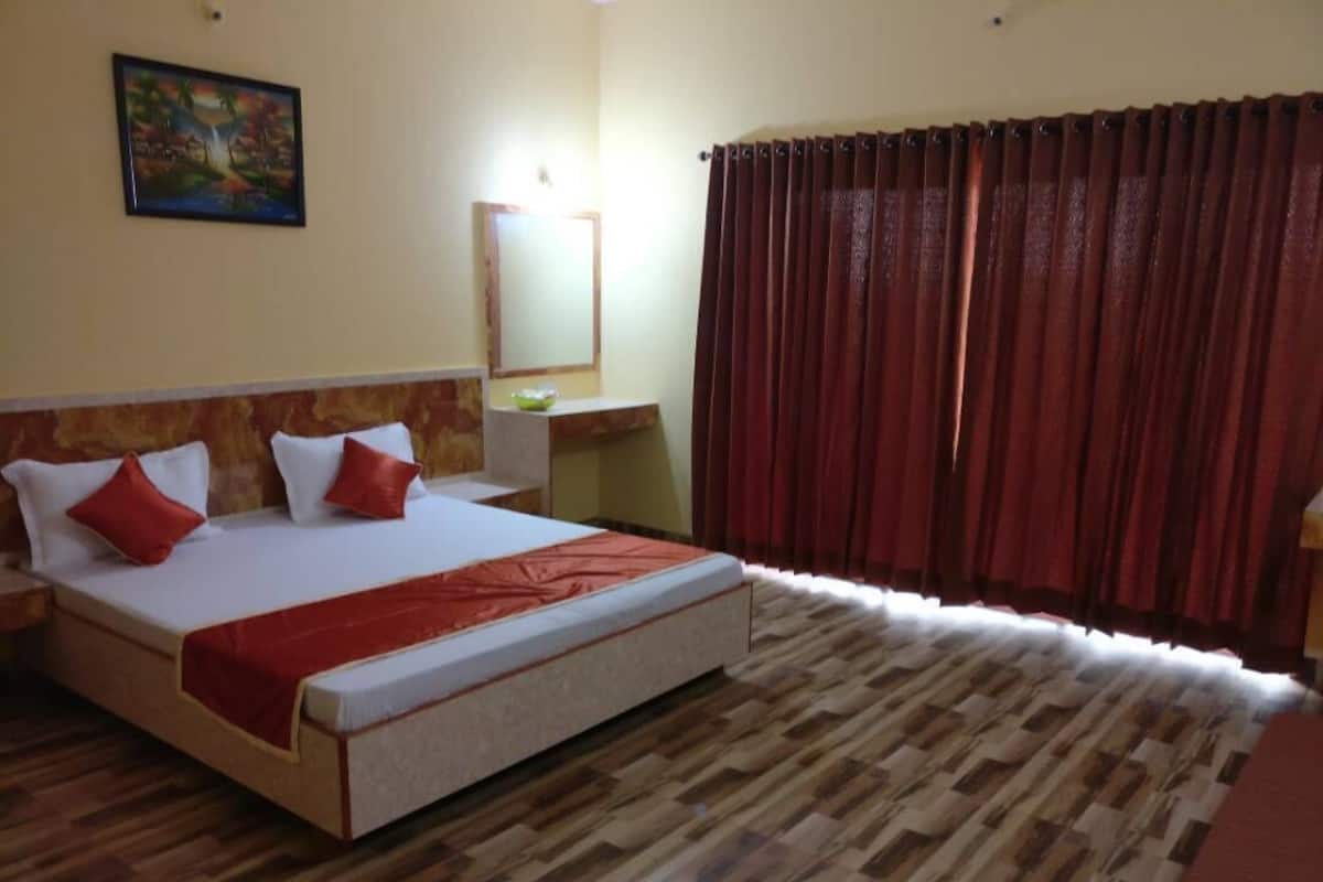 A hotel room with a bed, a desk, a mirror, and a window with curtains.