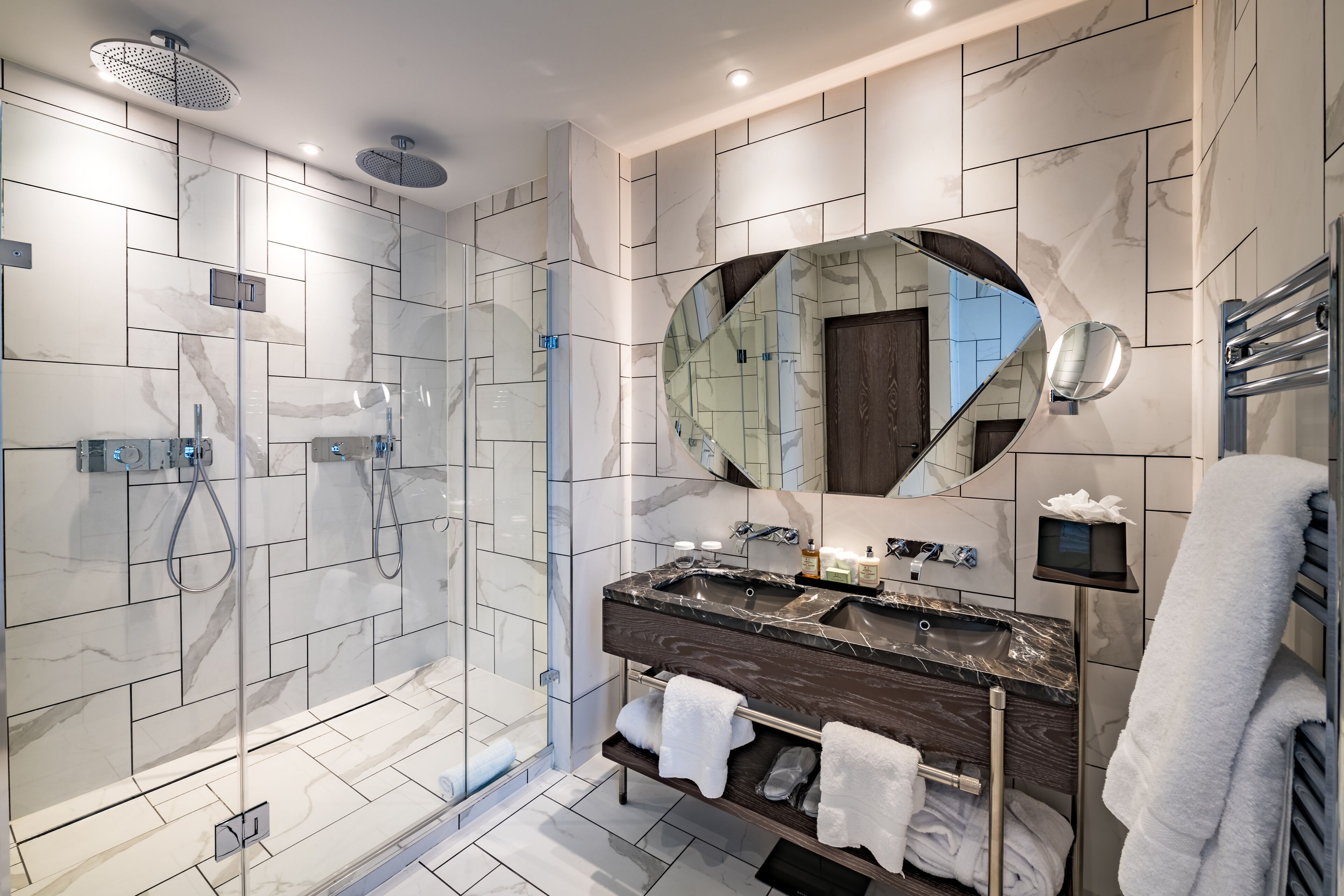 Un baño moderno con ducha de vidrio, tocador de madera oscura y un espejo grande.