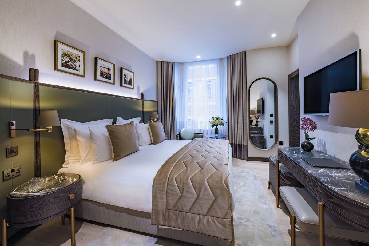 Una habitación de hotel moderna con una cama grande, un escritorio con televisión de pantalla plana, un espejo y cuadros en la pared.