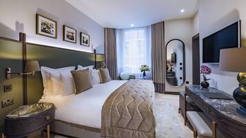 A modern hotel room with a large bed, a desk with a flat-screen TV, a mirror, and framed pictures on the wall.