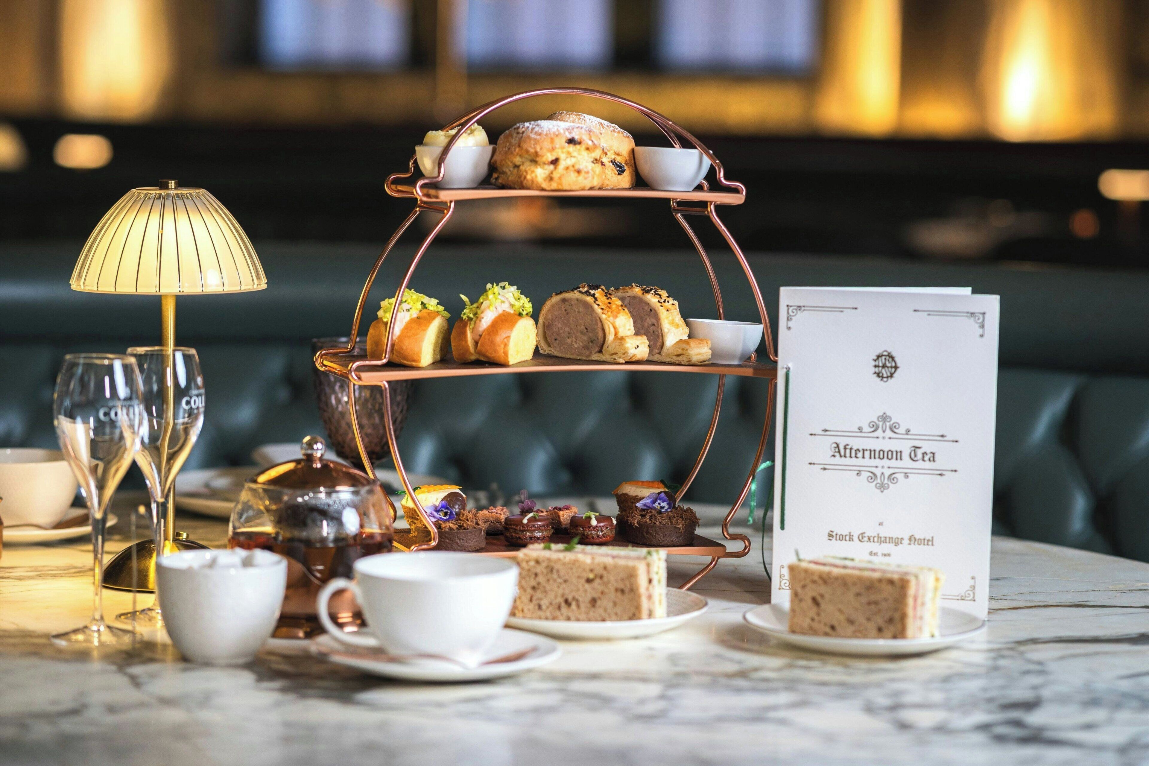 A tiered dessert stand with various pastries and a tea menu on a marble table.