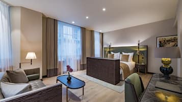 A modern hotel room with a bed, sofa, coffee table, and a desk with a lamp.