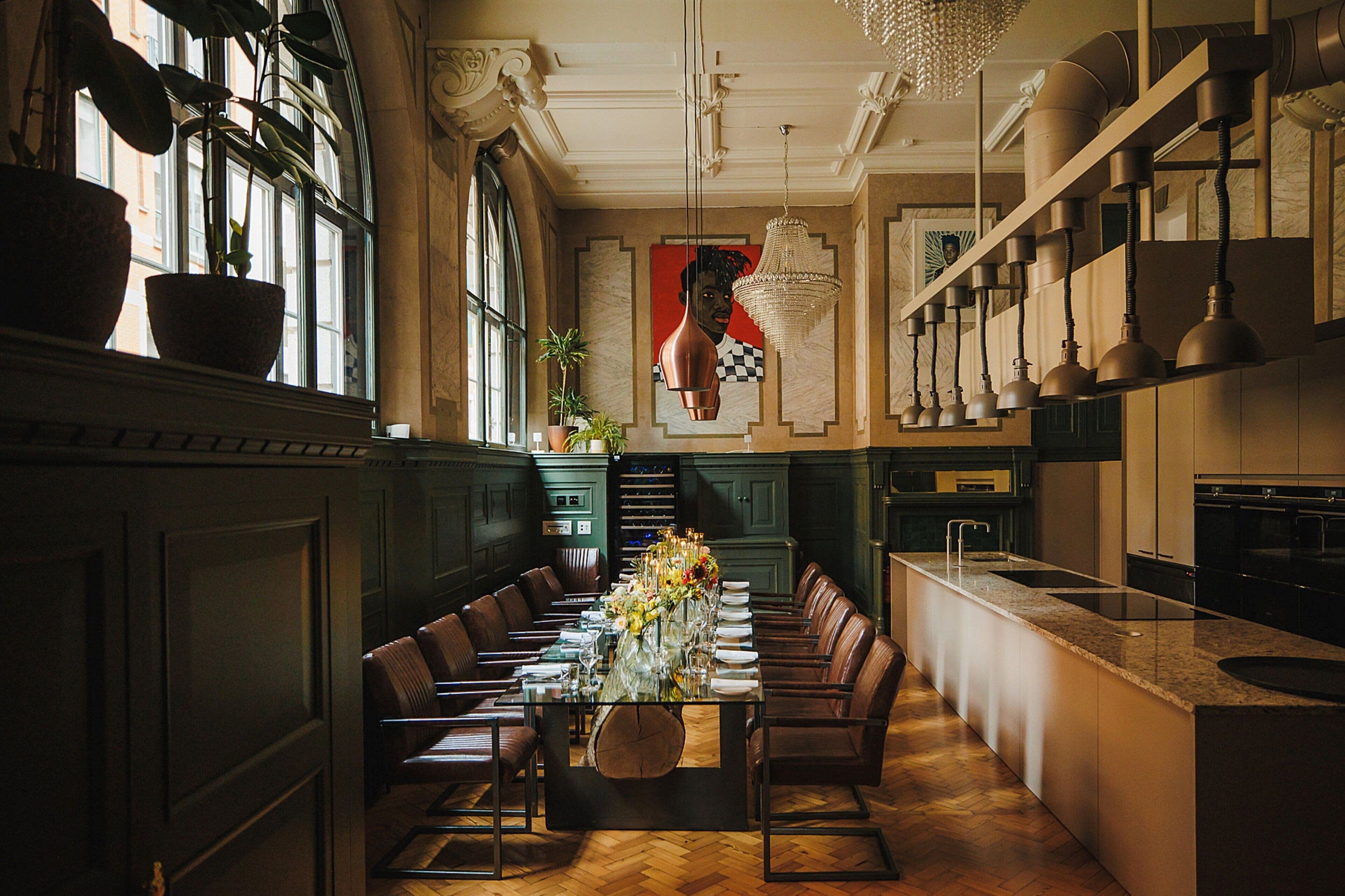 A spacious dining area with a long table set for a meal, surrounded by leather chairs, in a room with large windows and a chandelier.
