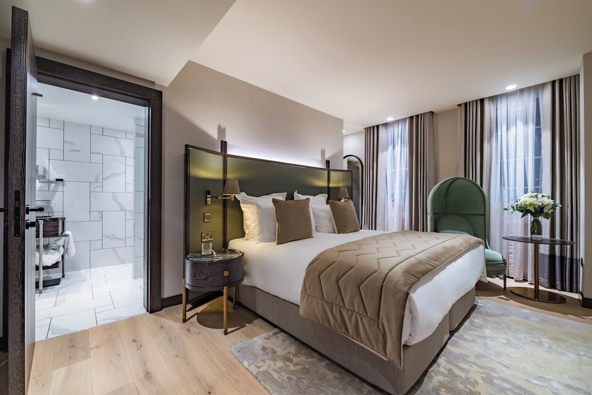 A modern hotel room with a large bed, a bedside table, a chair, and a view of the city through the window.