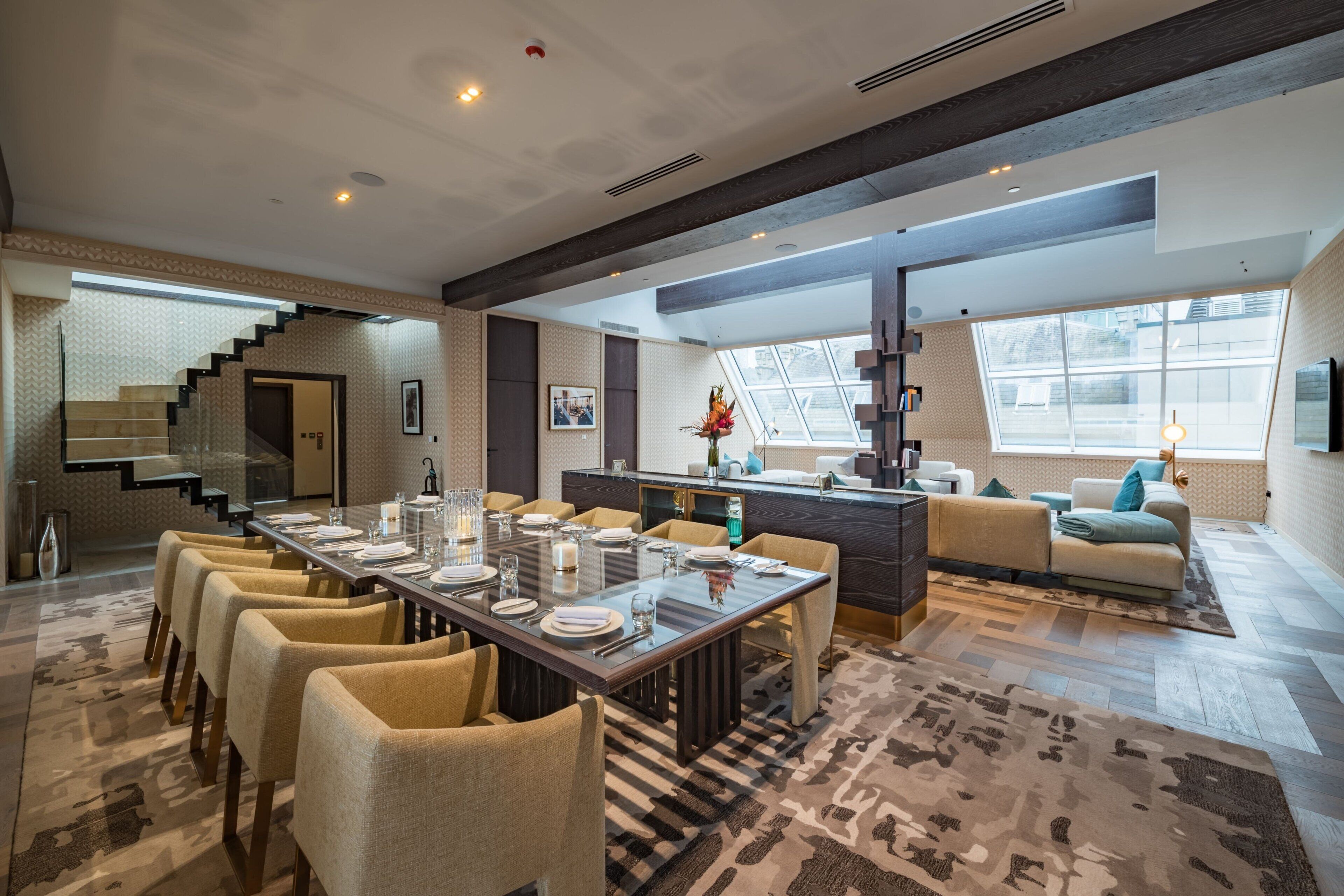 A modern dining area with a long table set for six, a staircase, and a cozy seating area with a sofa and armchairs.