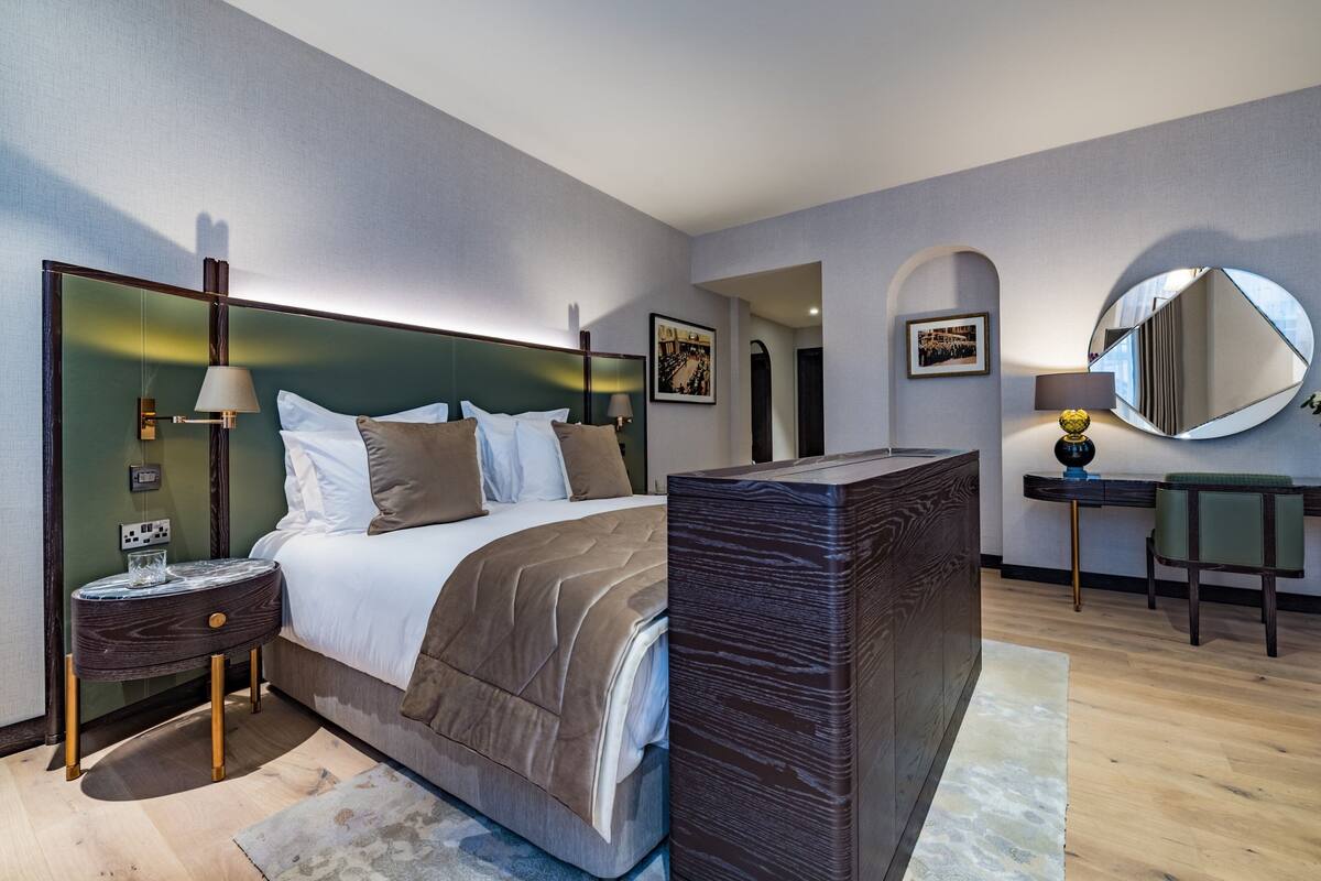 A modern hotel room with a large bed, a bedside table, a desk, and a mirror.
