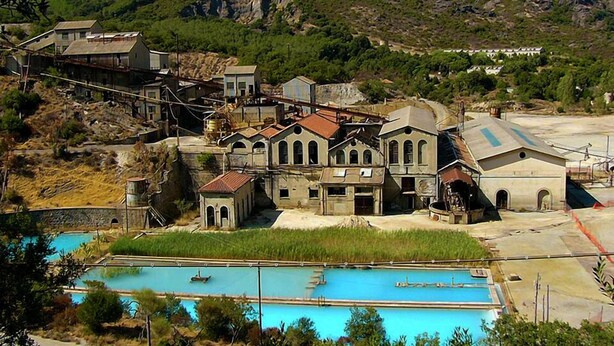 Un pueblo costero con edificios de piedra tradicionales, una piscina y un paisaje montañoso.