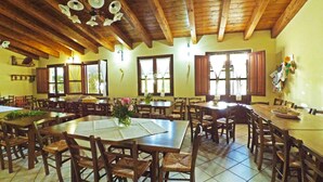Un comedor amplio con mesas y sillas de madera, ventanas grandes con cortinas y un alto techo de madera.
