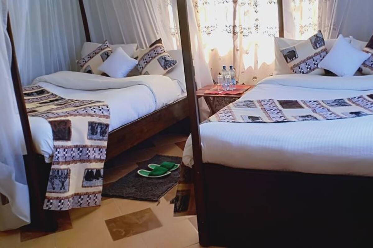 Dos camas con colchas estampadas, una mesita con botellas y un par de pantuflas en el suelo.