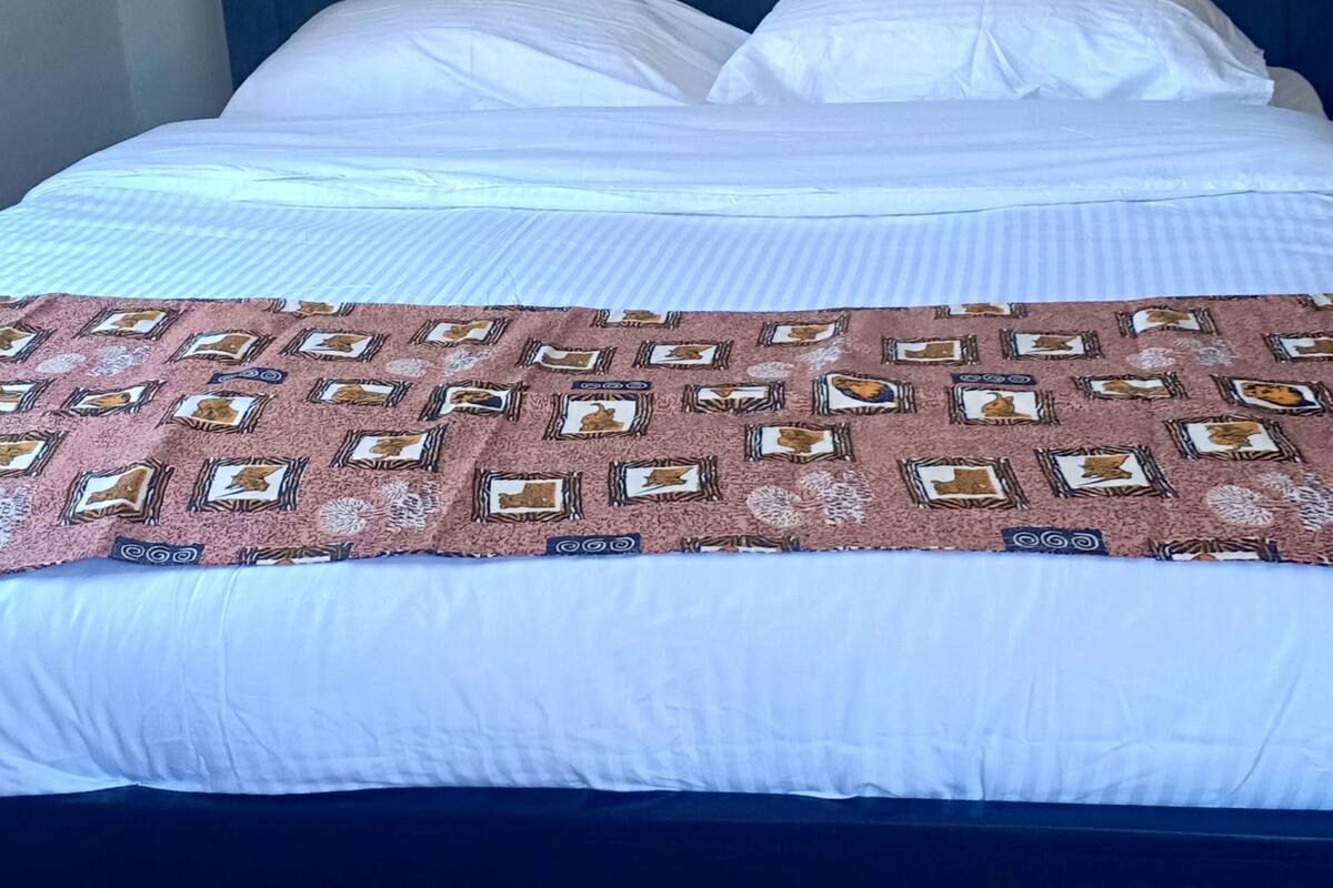 Una cama con colcha estampada, almohadas blancas y cabecera oscura.