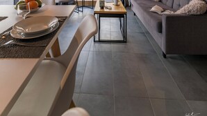 A modern living room with a sofa, dining table, and chairs. There is a window with curtains, a framed picture on the wall, and a view of trees outside. - Lagrange Vacances L'Ecrin du Badet (Aragnouet)
