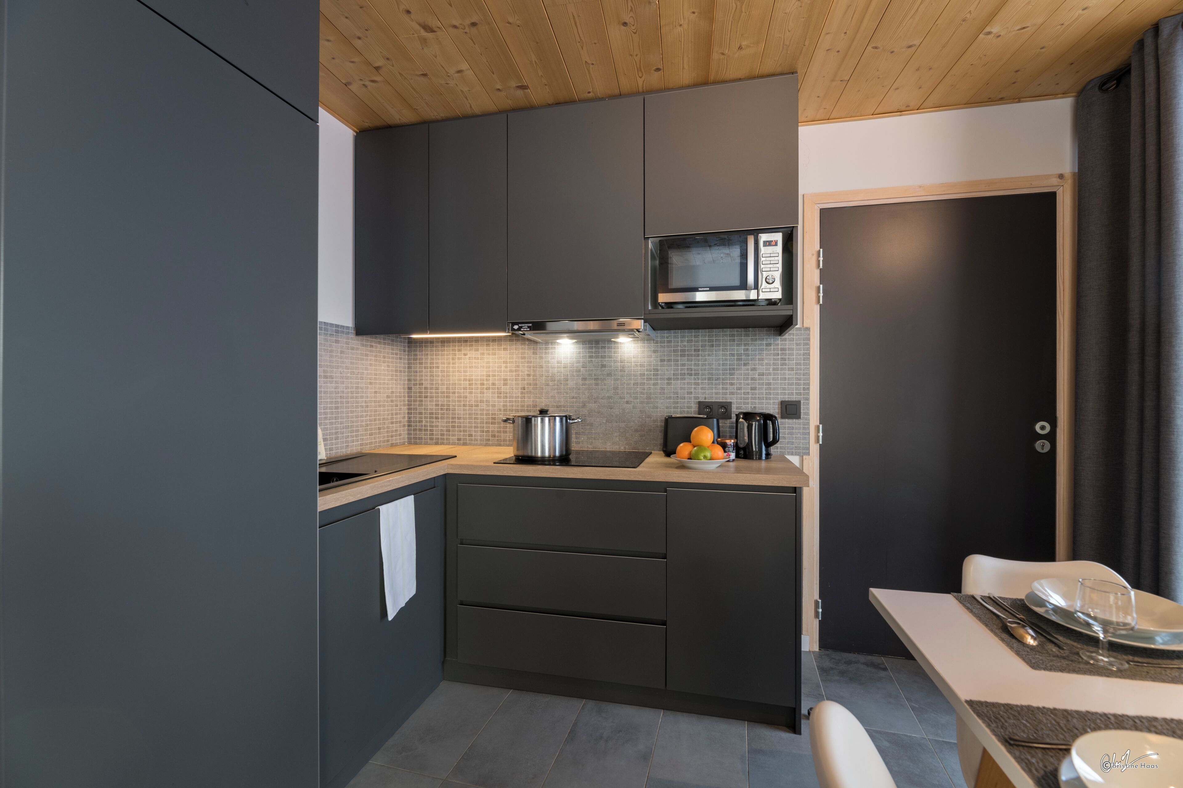 A modern kitchen with dark cabinetry, a microwave, and a stove. There is a dining area with a table set for two.