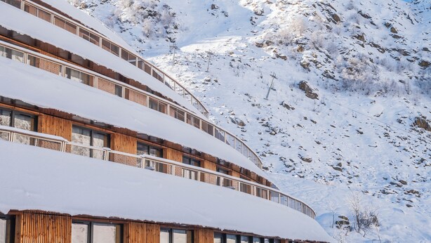 A multi-story building with a wooden facade and large windows, surrounded by snow-covered mountains. - Lagrange Vacances L'Ecrin du Badet (Aragnouet)