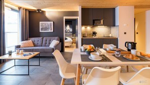 A modern living room with a grey sofa, a dining table with chairs, and a kitchen area with a microwave and coffee maker. - Lagrange Vacances L'Ecrin du Badet (Aragnouet)