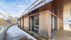 A modern building with a wooden deck and glass doors, overlooking a snowy mountain. - Lagrange Vacances L'Ecrin du Badet (Aragnouet)