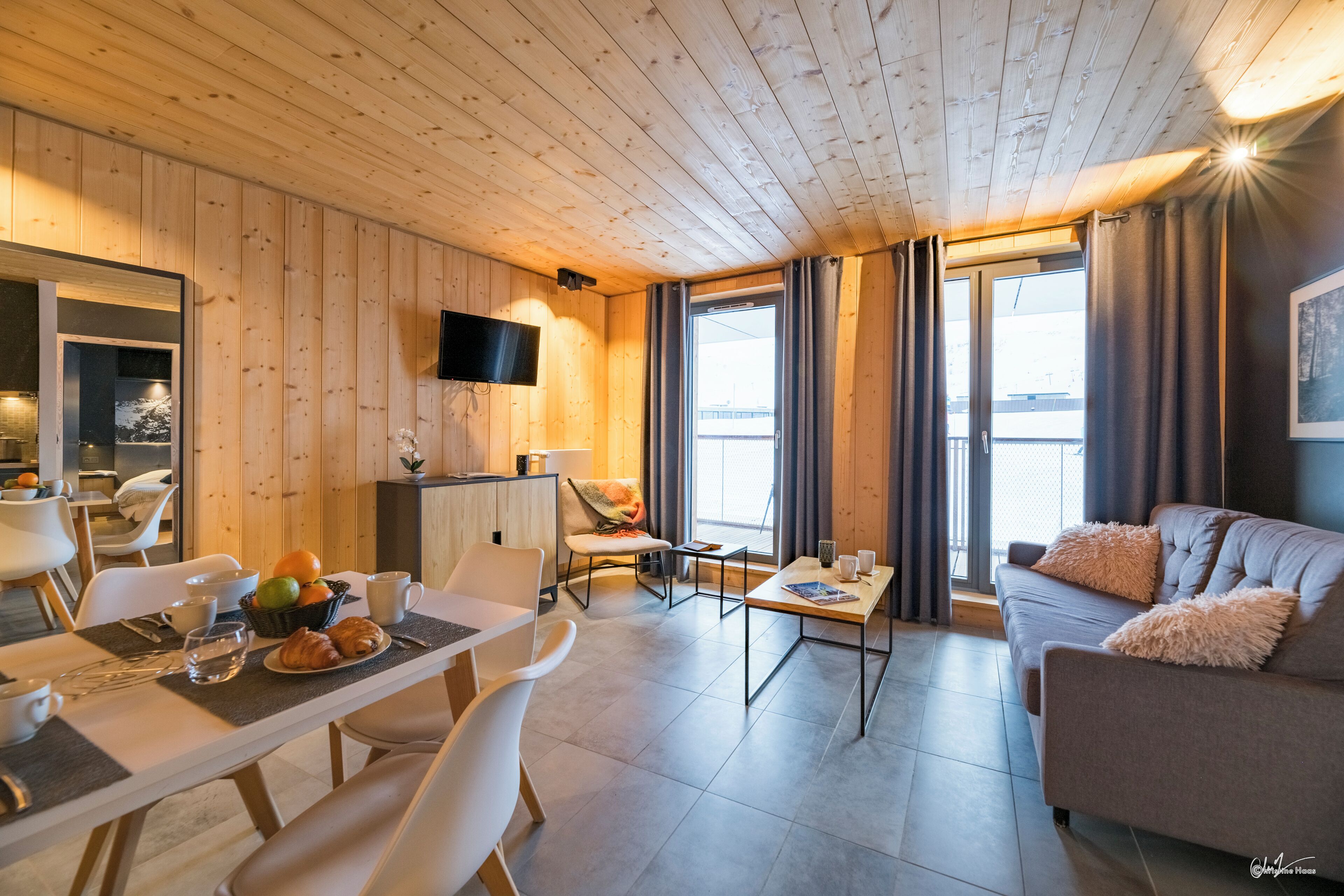 Ein modernes Interieur mit Holzbalkendecke, einer Essecke mit gedecktem Tisch für das Frühstück, einer Couch und einem an der Wand befestigten Fernseher.