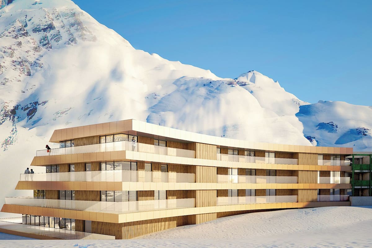 Un hôtel à plusieurs étages, doté d’un design moderne, avec des balcons et de grandes fenêtres, et qui se distingue sur fond de montagnes enneigées.