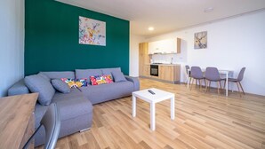 En moderne stue med en grå sofa, et hvidt sofabord og et køkken i baggrunden.
