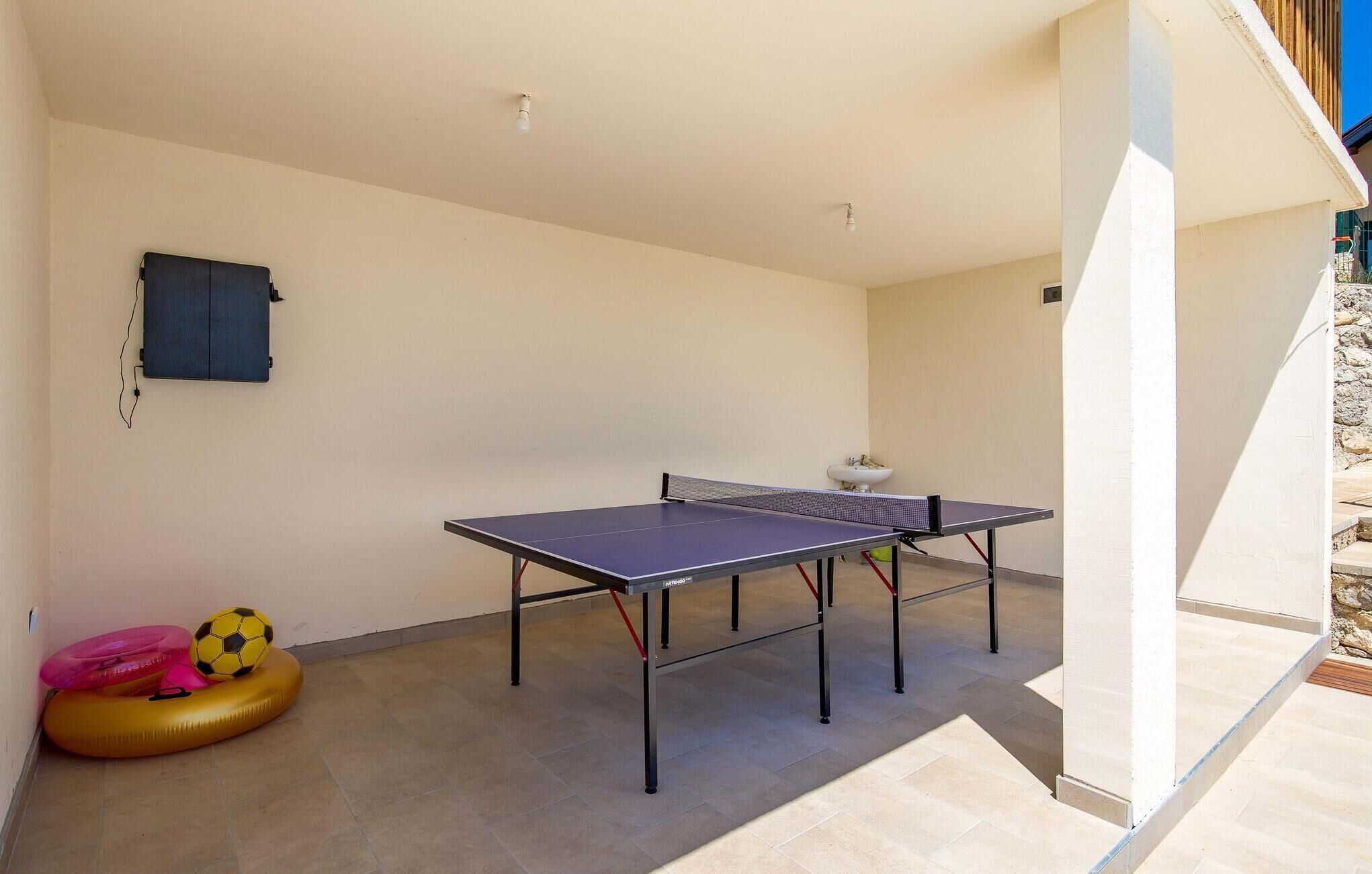 Una mesa de ping pong en una habitación con piso de baldosas, un armario empotrado en la pared y una pequeña planta.