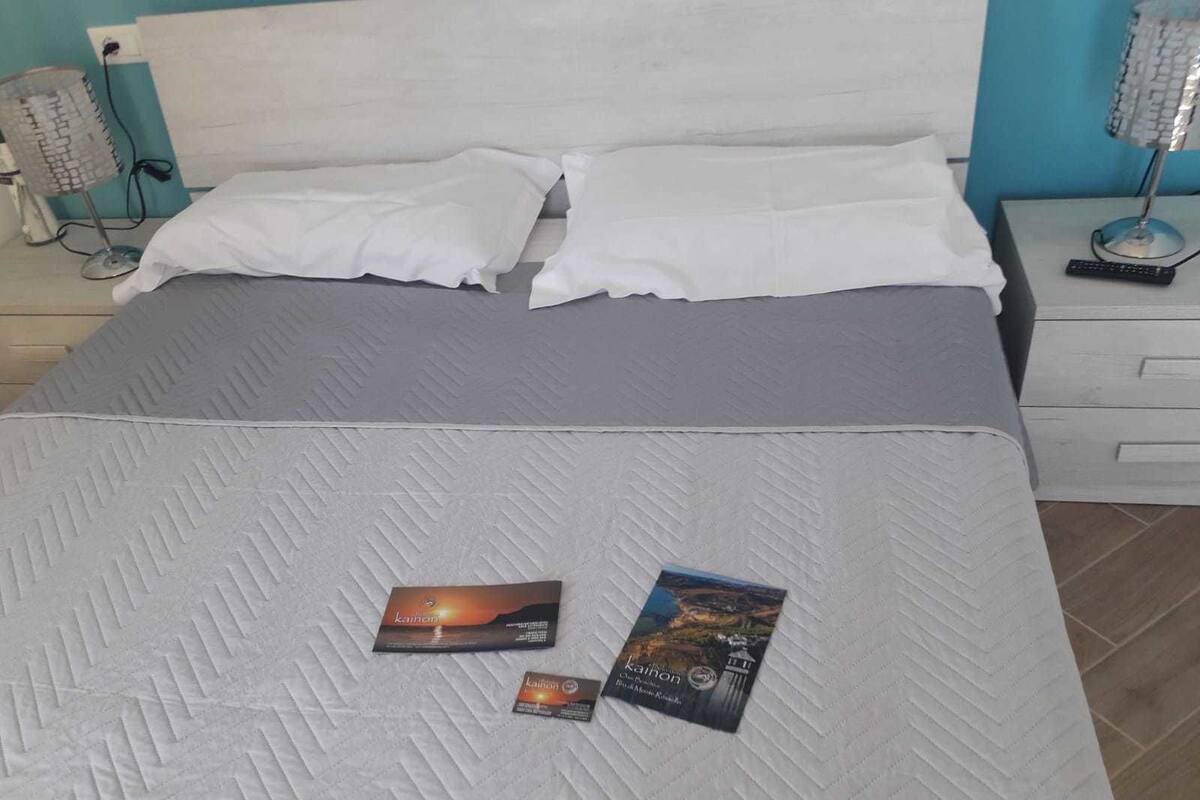 A neatly made bed with a grey quilt, two pillows, and two books on the bed.