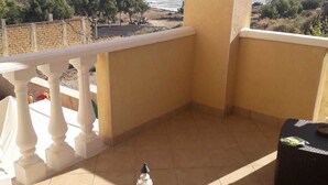Un balcón con vista al mar, una mesa pequeña con un cuenco y una botella, y una silla.