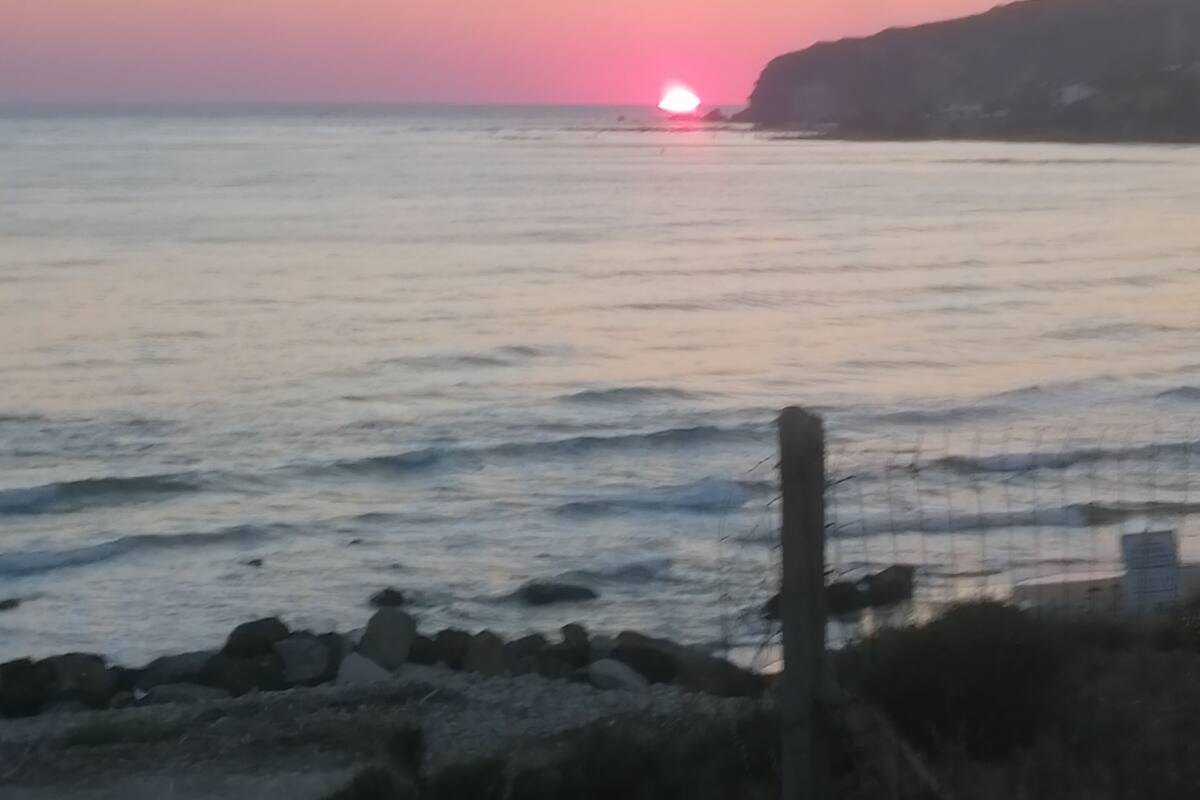 A coastal sunset view with calm waters and rocky shoreline.