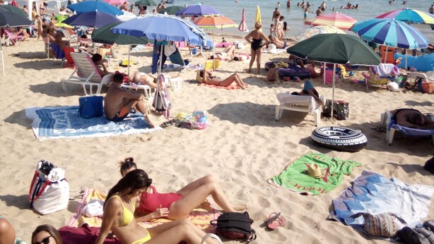Una playa concurrida, con muchas sombrillas y gente descansando sobre la arena.