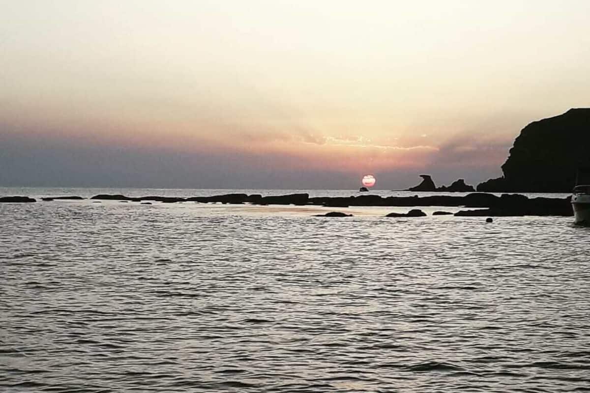 A coastal scene with calm water, a sunset, and rocky outcrops.