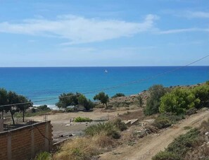 A coastal landscape with a clear view of the sea and a distant sailboat.