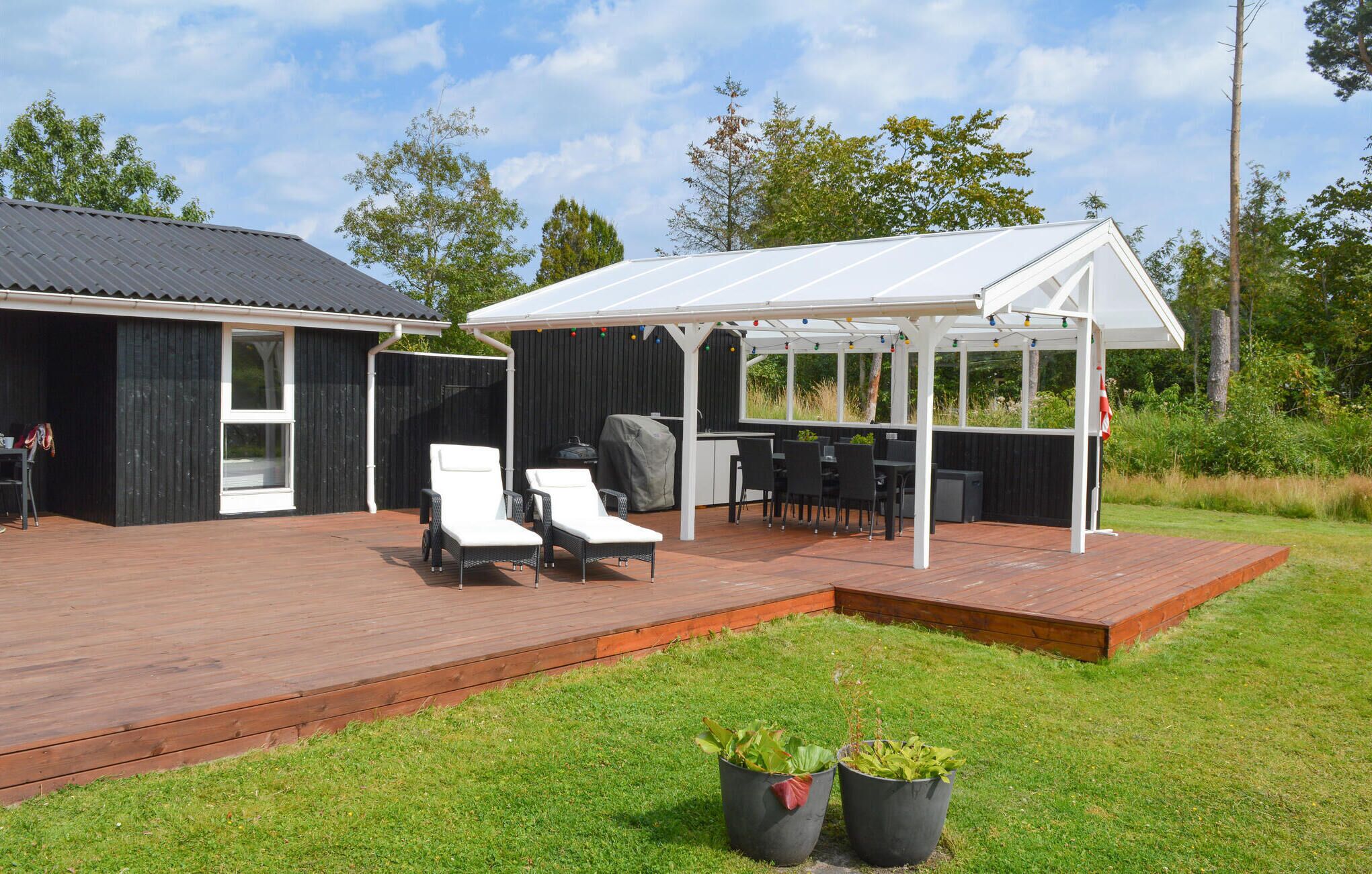 A covered outdoor area with a grill, lounge chairs, and a table.