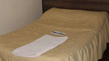 Una cama individual con una colcha color crema y una toalla blanca doblada encima.