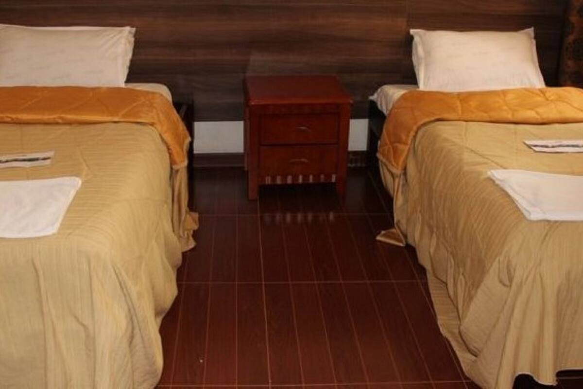 Twee enkele bedden met hoofdborden, een houten nachtkastje en een betegelde vloer.