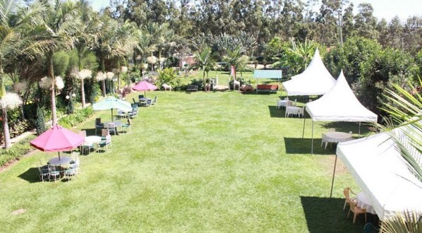 A well-maintained lawn with outdoor seating and white tents, surrounded by lush greenery and palm trees. - Gatimene Gardens Hotel (Meru)
