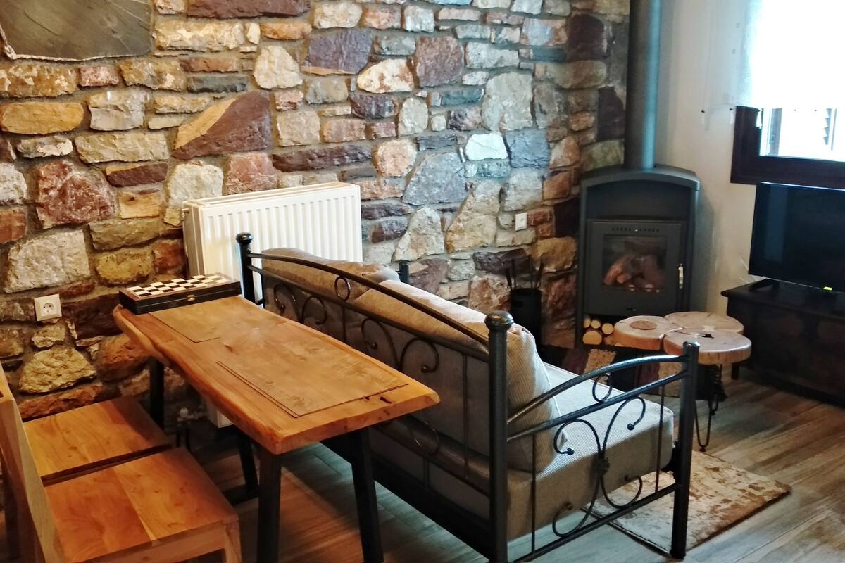 A cozy room with a stone wall, a fireplace, a wooden table, and a bench.