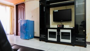 A living room with a black entertainment unit, a flat-screen TV, and a blue refrigerator. - 2BR Apartment at Great Western Serpong (Tangerang)