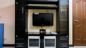 A black entertainment unit with a flat-screen TV, a travel adapter, and a small table. - 2BR Apartment at Great Western Serpong (Tangerang)