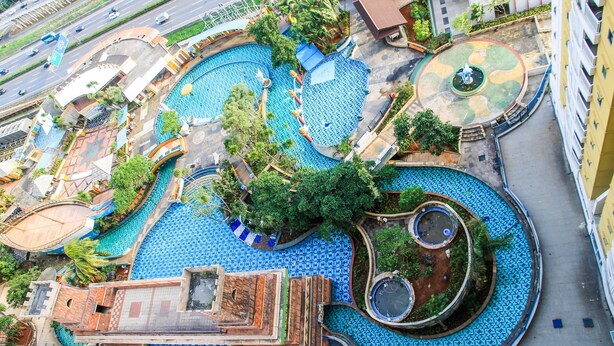 An aerial view of a hotel with multiple swimming pools, a central fountain, and surrounding greenery. - 2BR Apartment at Great Western Serpong (Tangerang)