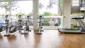 A gym with exercise equipment, a wooden floor, and a view of parked cars and trees outside.