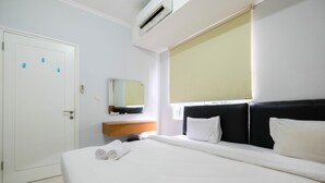 A hotel room with a bed, a bedside table, a mirror, and a window with a blind.