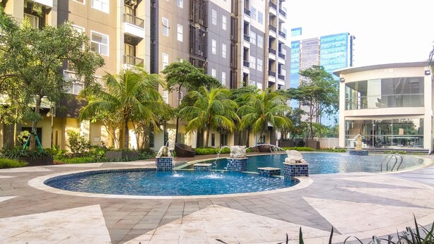 A modern apartment complex with a central swimming pool surrounded by palm trees and a landscaped garden.