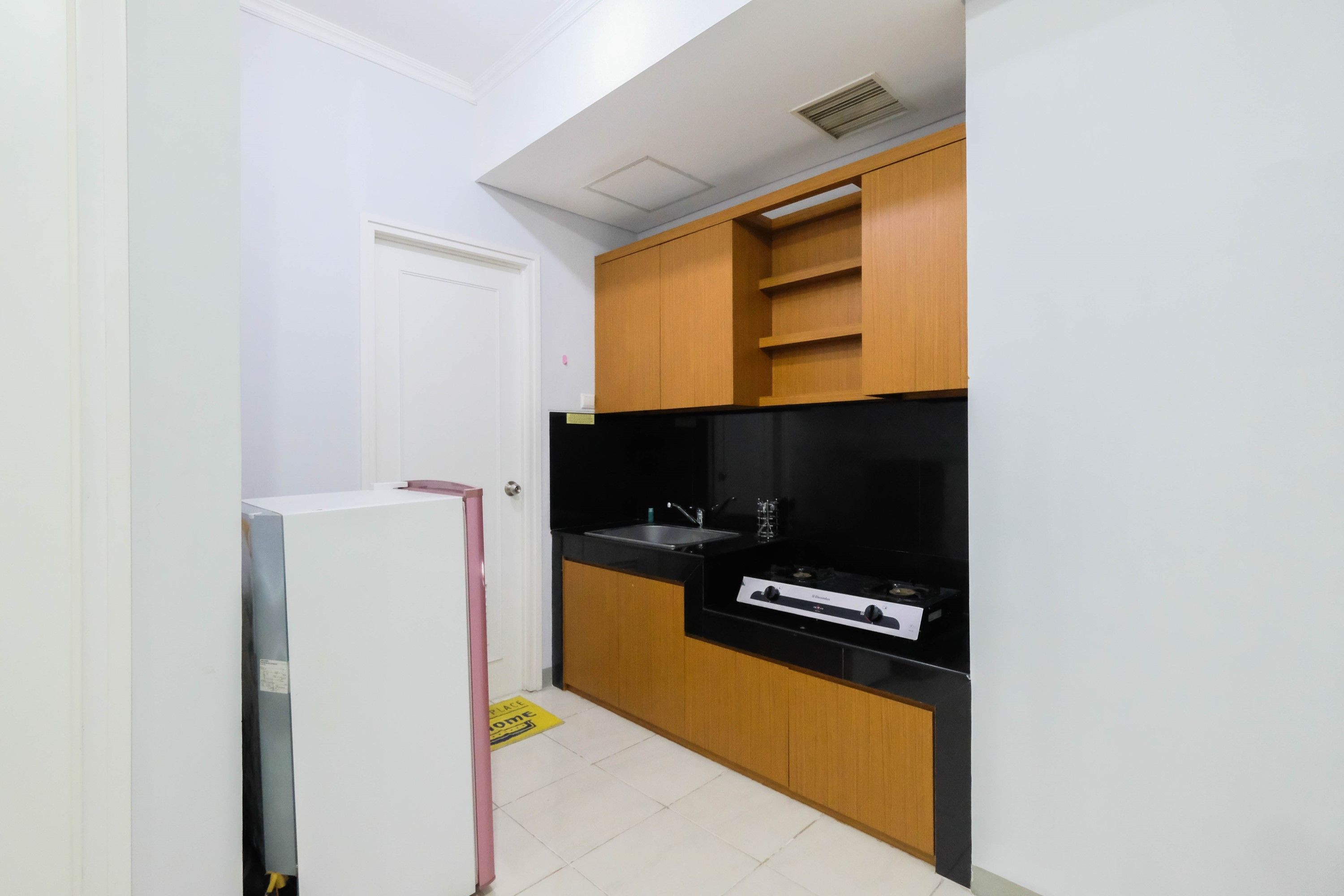 A compact kitchen with wooden cabinets, a black countertop, and a stainless steel sink.