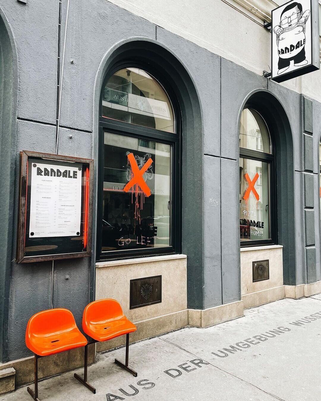 Een gebouw met een bord waarop 'RANDALE' staat en twee oranje stoelen voor de deur.