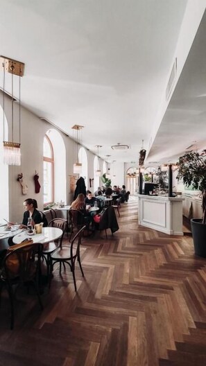 A spacious restaurant with high ceilings and wooden flooring, featuring tables and chairs arranged for dining. - Hotel Babula am Augarten (Vienna)