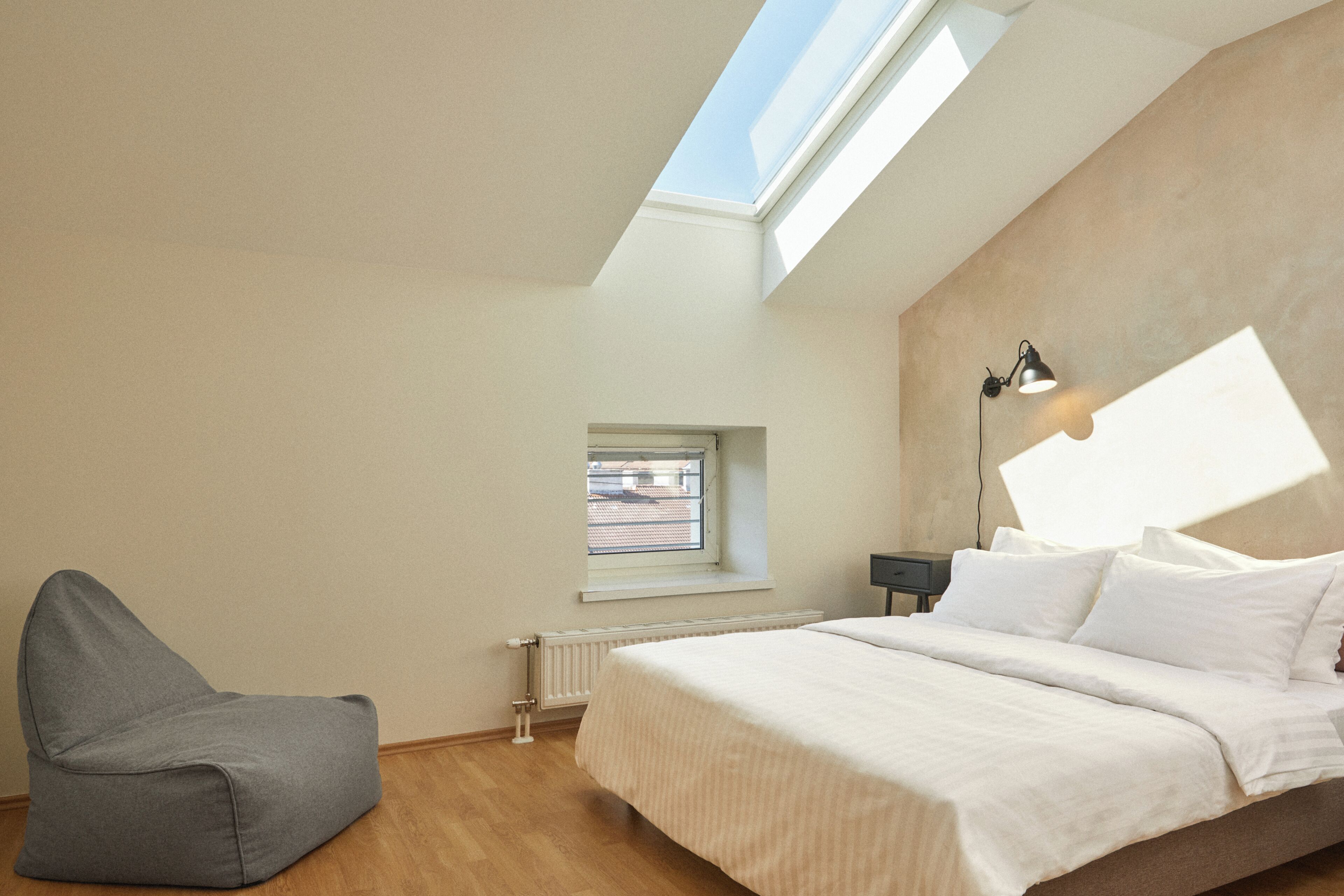 A bedroom with a skylight, a window, a bed, a bedside table, and a chair.