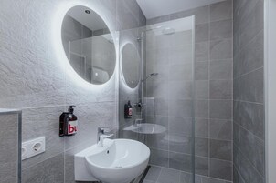 Uma casa de banho moderna com uma sanita branca, uma cabine de duche com parede de vidro e um espelho redondo com luz.