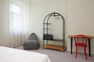 Quarto com uma cama, uma poltrona de feijão cinza, uma cadeira vermelha, uma escrivaninha de madeira e uma estante de metal preta.