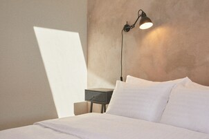 A neatly made bed with white linens, a bedside table with a lamp, and a wall with a textured finish.