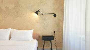 Een slaapkamer met een bed, kussens, een nachtkastje, een lamp en een stopcontact.