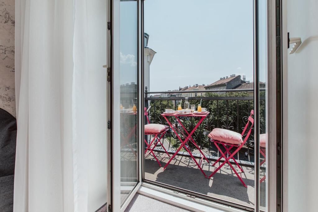 Een balkon met een glazen deur, rode opklapstoelen en een kleine tafel met een kopje en schoteltje.