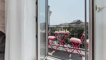 Een balkon met een glazen deur, rode opklapstoelen en een kleine tafel met een kopje en schoteltje.